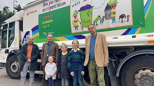 6 People standing in front of a waste vehicle.